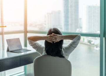 Lady at work leaning back on her chair staring out of the window, thinking of work-life balance