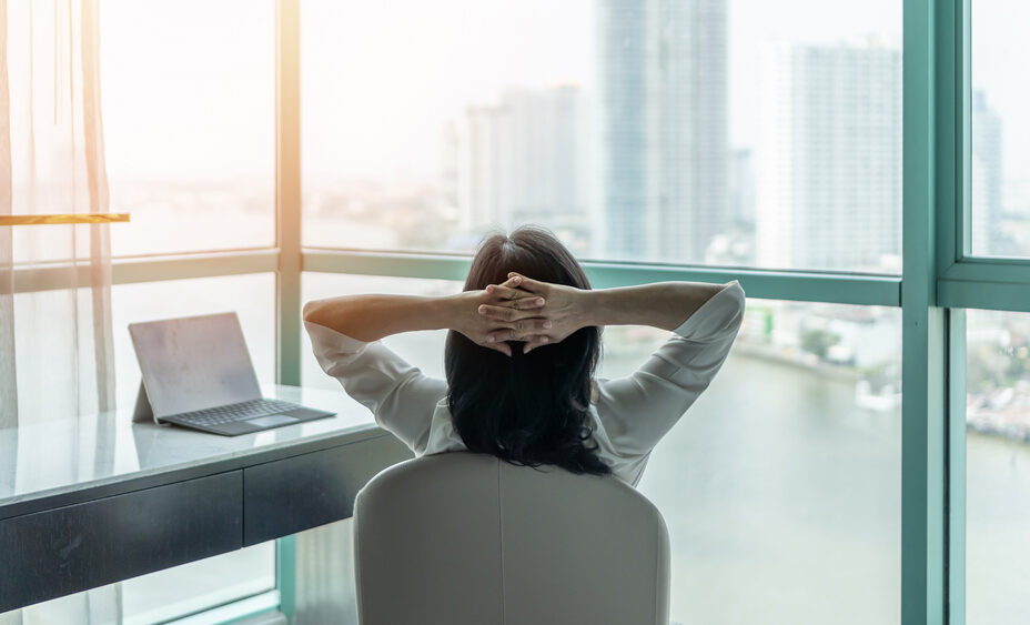 Lady at work leaning back on her chair staring out of the window, thinking of work-life balance